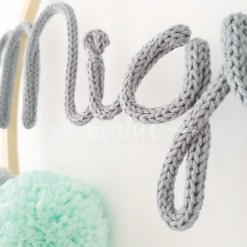 Caça sonhos artesanal em bastidor de madeira natural com nome personalizado, decorado com pompons e fios de lã, ideal para a decoração de quarto infantil