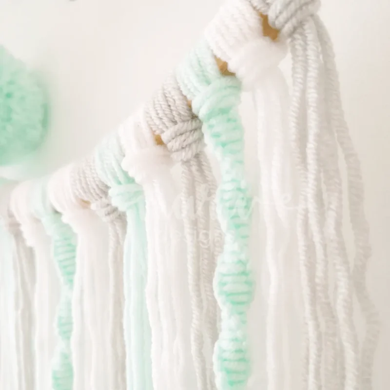 Caça sonhos artesanal em bastidor de madeira natural com nome personalizado, decorado com pompons e fios de lã, ideal para a decoração de quarto infantil