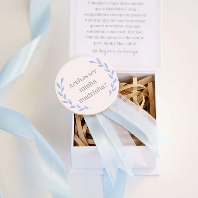 Caixa convite personalizada com mensagem para madrinha ou padrinho, decorada com fita de cetim e detalhe de medalhão em madeira com a inscrição 'Aceitas ser minha madrinha/padrinho?'