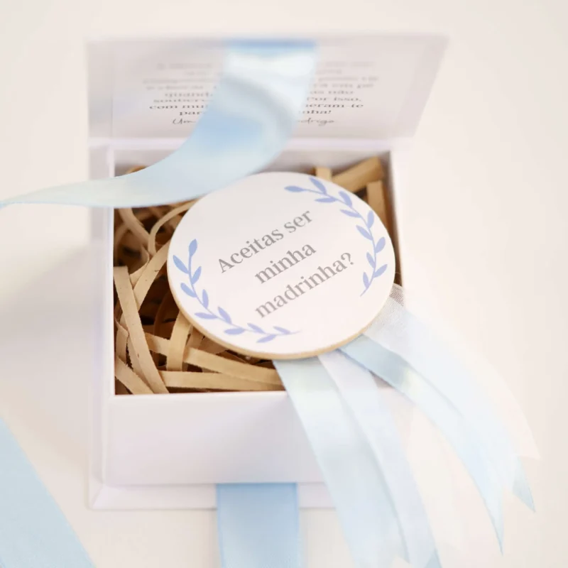 Caixa convite personalizada com mensagem para madrinha ou padrinho, decorada com fita de cetim e detalhe de medalhão em madeira com a inscrição 'Aceitas ser minha madrinha/padrinho?'