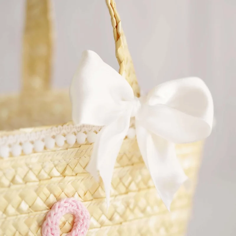 Mala de palha para criança decorada com inicial em crochet, laço branco e detalhes delicados