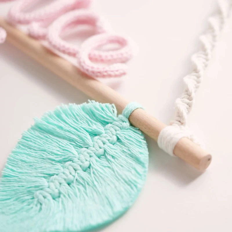 Decoração infantil com o nome personalizado em crochet, pendurado num suporte de madeira com corda em macramé e uma folha decorativa verde em macramé