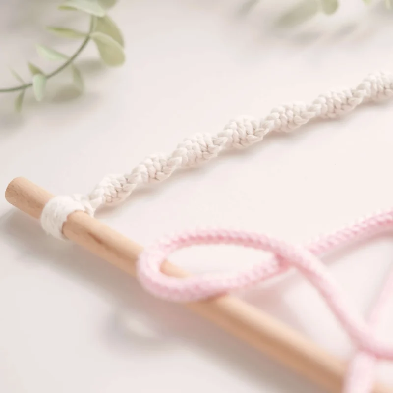 Decoração infantil com o nome personalizado em crochet, pendurado num suporte de madeira com corda em macramé e uma folha decorativa verde em macramé