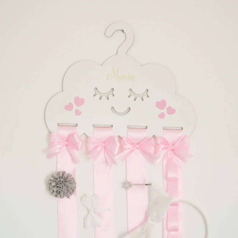 Porta laços em formato de nuvem branca com fitas de cetim rosa, detalhes de laços decorativos e espaço para organizar acessórios infantis