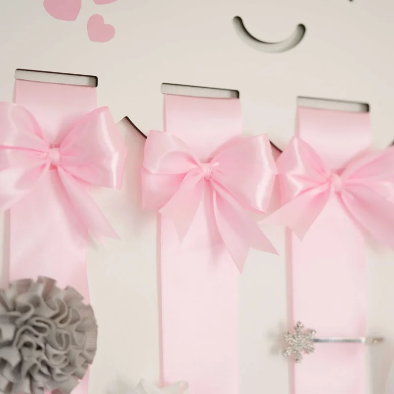 Porta laços em formato de nuvem branca com fitas de cetim rosa, detalhes de laços decorativos e espaço para organizar acessórios infantis