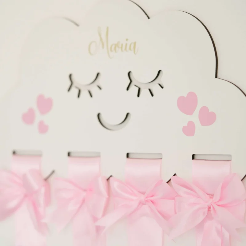 Porta laços em formato de nuvem branca com fitas de cetim rosa, detalhes de laços decorativos e espaço para organizar acessórios infantis