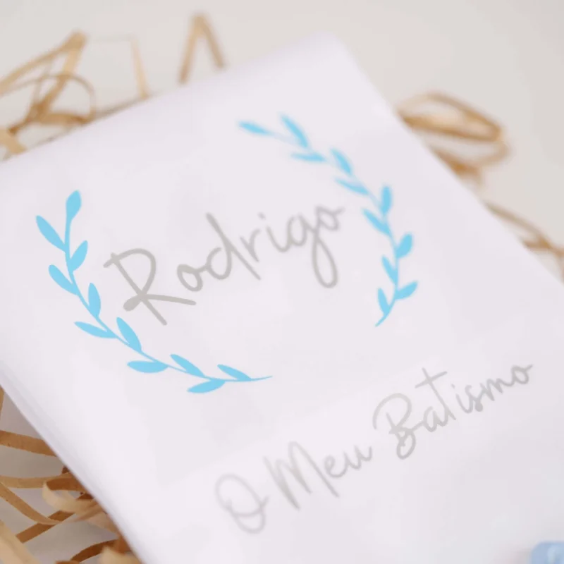 Toalha de Batismo personalizada com estampagem, decorada com renda e um laço delicado, exibindo o nome da criança e a frase 'O Meu Batismo'